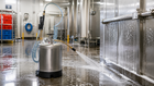 Portable stainless steel chemical sprayer applying cleaning solution to industrial equipment in a food-processing facility.