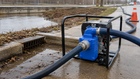 Portable engine-driven water pump draining stormwater through large suction and discharge hoses.
