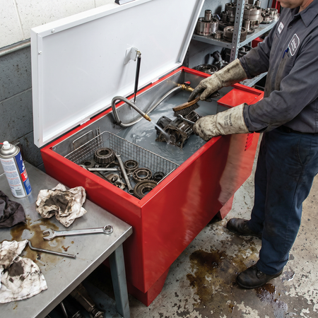 Operator cleaning mechanical components inside the Leg Mount Solvent Washer tank.